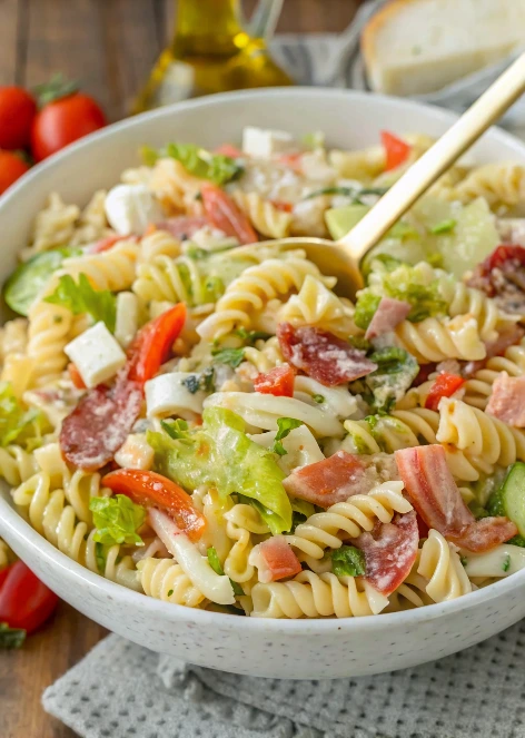 Grinder-style Italian pasta salad served in a white bowl, filled with colorful vegetables, sliced meats, and fresh mozzarella balls.
