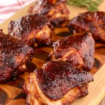 Six juicy smoked chicken thighs resting on a wooden cutting board with a text overlay that reads 'Smoked Chicken Thighs'